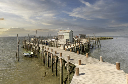 A weathered wooden pier and small hut extend into a tranquil river, with a lone boat anchored nearby.の写真素材