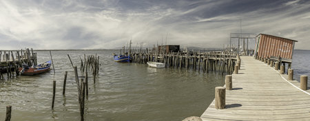 A weathered wooden pier and small hut extend into a tranquil river, with a lone boat anchored nearby.の写真素材