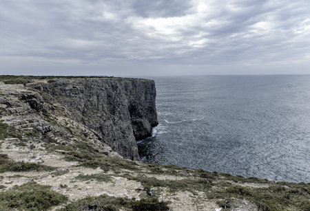 A dramatic coastal landscape featuring rugged cliffs and a rocky shoreline at Cape St. Vincent,...