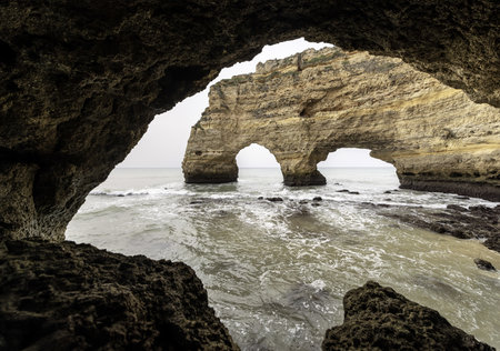 A rocky outcrop at Marinha Beach, Portugal, silhouetted against the soft light of a cloudy sky. Waves gently lap at the shore, creating a serene coastal scene.の写真素材