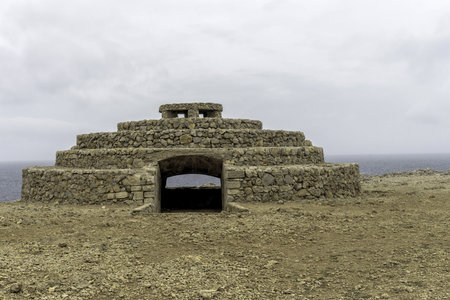Historic Punta Nati anti-aircraft battery in Menorca, showcasing a tiered stone structure under an overcast sky. The rugged coastal landscape adds to the historic atmosphere.の写真素材