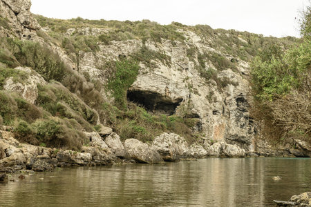 A rugged, rocky inlet at Cala Coves, Menorca, showcasing dramatic cliffs and natural caves. The calm, clear waters enhance the wild, untouched beauty of this unique coastal landscape.の写真素材