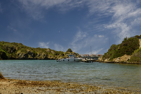 Scenic view of Cala Escull harbor in Menorca, featuring anchored boats, clear blue waters, and a...