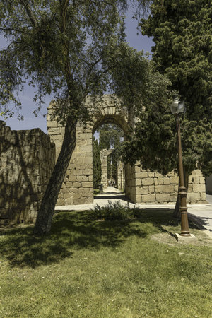 Historic Roman city walls in Merida, Spain, surrounded by lush trees and a paved walkway. The preserved stone structures reflect the city's rich ancient heritage under a bright blue sky.の写真素材