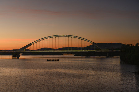 The Lusitania Bridge in Merida, Spain, silhouetted against a stunning sunset over the Guadiana River.の写真素材
