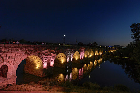 The ancient Roman bridge over the Guadiana River in Merida, Spain, beautifully illuminated at dusk.の写真素材