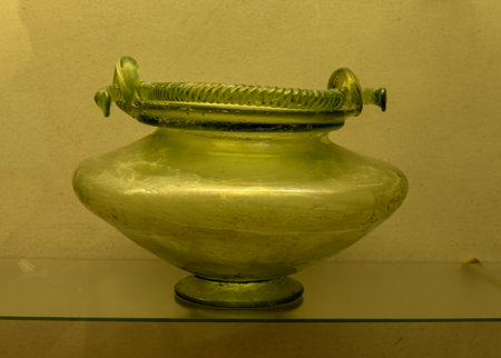 An ancient Roman green glass vase with intricate design. Features a wide body, a narrow neck, and decorative handles, showcasing Roman glassmaking craftsmanship.の写真素材