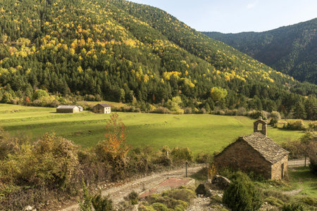 A rustic stone chapel with a slate roof, nestled in a picturesque valley with vibrant forested hills in the background.の写真素材