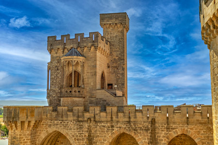 Medieval castle tower with crenellated walls, stone arches, and architectural details against a vibrant blue sky.の写真素材