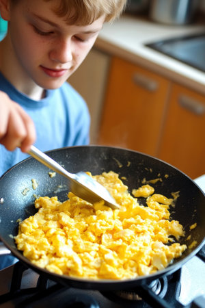 A young boy preparing scrambled eggs in a frying pan, focused on cooking in a kitchen setting.の素材
