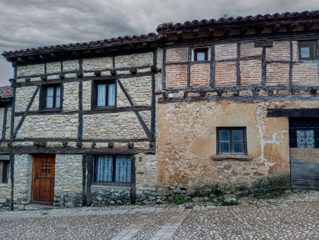 Traditional half-timbered houses with stone walls line a cobblestone street in a historic village in Soria, Spain.の写真素材