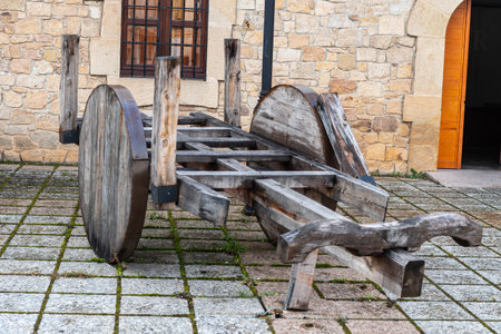 A traditional wooden cart with large wheels, placed on a cobbled street in Soria, Spain, near a stone wall and a lamppost.の写真素材