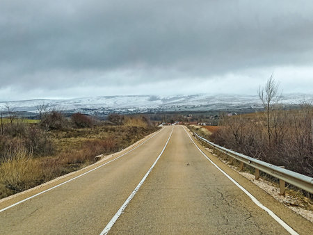 Long straight road heading to Yanguas, Soria, surrounded by countryside, with snow-covered mountains...
