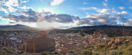 A panoramic view of Arnedo, La Rioja, Spain, showing a historic town with terracotta-roofed houses, a medieval castle on a hill, and a church under a cloudy sky.の写真素材
