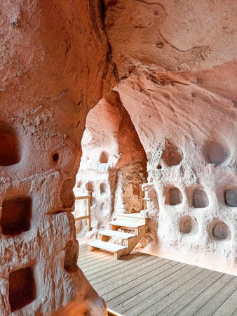 A rock-carved chamber inside the Cave of the Hundred Pillars in Arnedo, La Rioja, Spain, featuring hand-carved niches, textured stone walls, and wooden stairs leading to another section.の写真素材