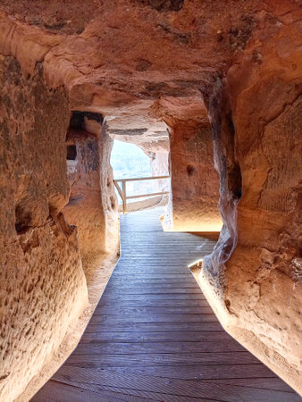 A rock-carved chamber inside the Cave of the Hundred Pillars in Arnedo, La Rioja, Spain, featuring hand-carved niches, textured stone walls, and wooden stairs leading to another section.の写真素材