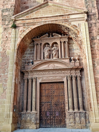 A close-up of the entrance to the Iglesia de San Cosme y San Damian in Arnedo, La Rioja, Spain, showing intricate stone carvings, twisted columns, and a wooden door with iron studs.の写真素材