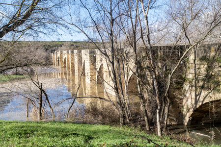 Ancient stone bridge with multiple arches spanning the Ebro River in San Vicente de la Sonsierra, Spain, surrounded by natural landscapes and vineyards.の写真素材