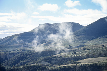 A breathtaking view of Sierra Magina, Spain, featuring mist rising over olive groves and mountainous...