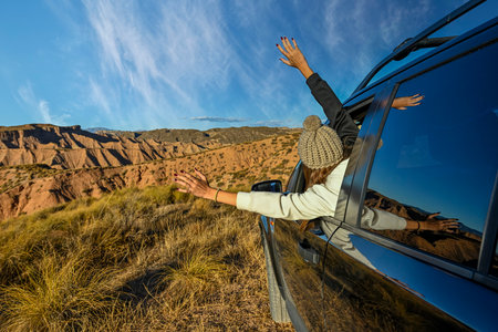 Young girl sticking her arms out of the car window, in the middle of a desert landscapeの写真素材