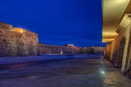 Massive stone bastions of the Murallas Reales in Ceuta reflected in a calm moat at dusk.の写真素材
