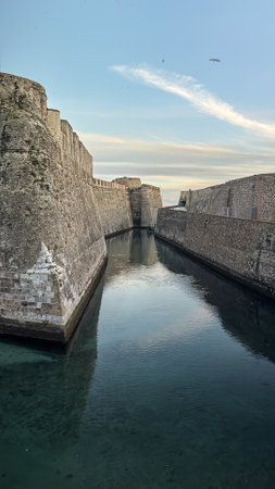 Massive stone bastions of the Murallas Reales in Ceuta reflected in a calm moat at dusk.の写真素材