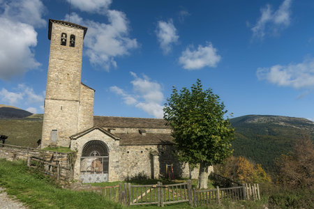 A historic stone church with a bell tower, surrounded by greenery and set against a bright blue sky...