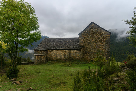 Romanesque stone church undergoing restoration, located in a lush rural area surrounded by forested hills and greenery.の写真素材