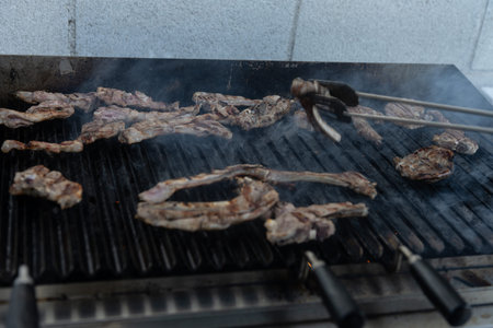 Juicy lamb chops cooking on barbecue grill with smoke and utensil holding a slice.