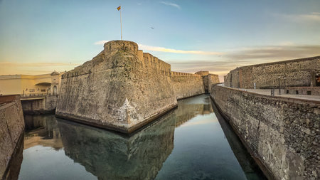 Massive stone bastions of the Murallas Reales in Ceuta reflected in a calm moat at dusk.の写真素材