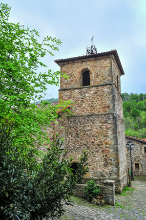 An ancient stone bell tower rises above the foliage in a historic European village, showcasing medieval architectureの写真素材