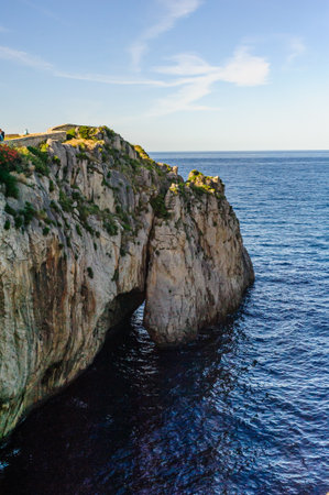 A natural limestone cliff majestically towers over the serene blue sea waters under a clear skyの写真素材