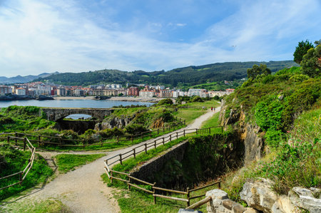 A picturesque walking path along the rocky coastline with views of Castro Urdiales town and lush hills in the background.の写真素材