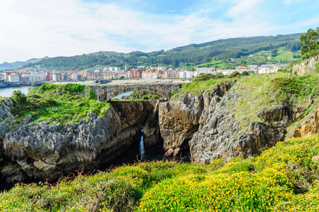 A picturesque walking path along the rocky coastline with views of Castro Urdiales town and lush hills in the background.の写真素材