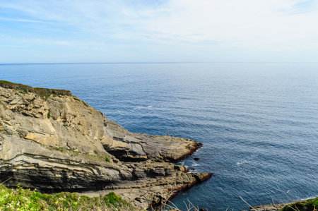 Striking layered rock formations along the rugged coast of Northern Spain with a clear blue sky overhead.の写真素材