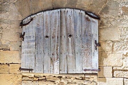 A weathered wooden door with iron hardware, set within a textured stone wall, evoking rustic charm.の写真素材