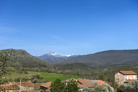Picturesque landscape featuring a small village, rolling hills, and snowy peaks in the distance.