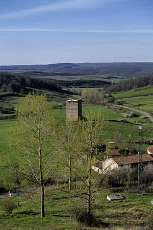 Old defensive stone tower in a rural landscape surrounded by green hills and traditional rooftops.の写真素材