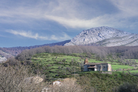 Old stone church with bell gable in a green valley and mountainous backdrop.の写真素材