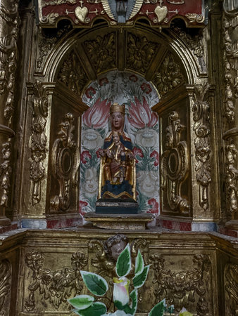 Ancient wooden statue of the Virgin Mary holding the Child Jesus, set on a golden baroque altar.の写真素材