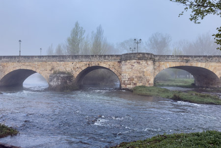 Historic Romanesque bridge spanning the Pisuerga River in Aguilar de Campoo, Palencia, Spain.