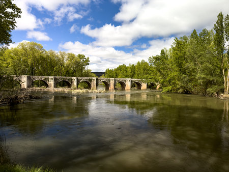 This image captures the Renaissance bridge crossing the Arlanza River in Quintana del Puente,...