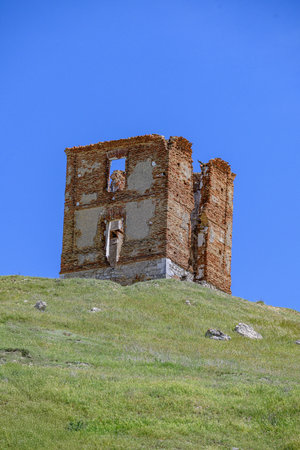 Remains of an old brick tower standing on a green hill with a vivid blue sky
