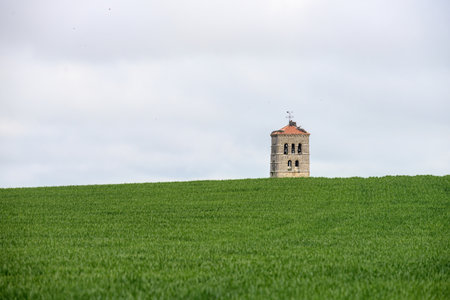 Tall medieval bell tower of a Romanesque rural church surrounded by cultivated fieldsの写真素材