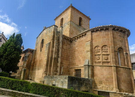 Beautiful Romanesque stone church with intricate arch details and a bell tower, surrounded by a peaceful urban area.の写真素材