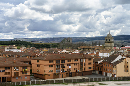 Wide view of Aguilar de Campoo with rooftops, fields, and mountains under stormy clouds.の写真素材