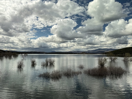 Peaceful lakeside landscape with still water and dramatic clouds over mountainsの写真素材