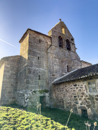 Ancient stone church surrounded by hills and rustic walls under clear blue skyの写真素材