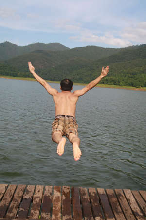 a asia man jump to lake water with mountain view background の写真素材