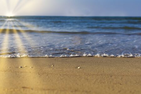 Soft wave from sea come to wet sand beach with blur clear sky and sun ray background. With copy space for text or design. Beach background.の写真素材